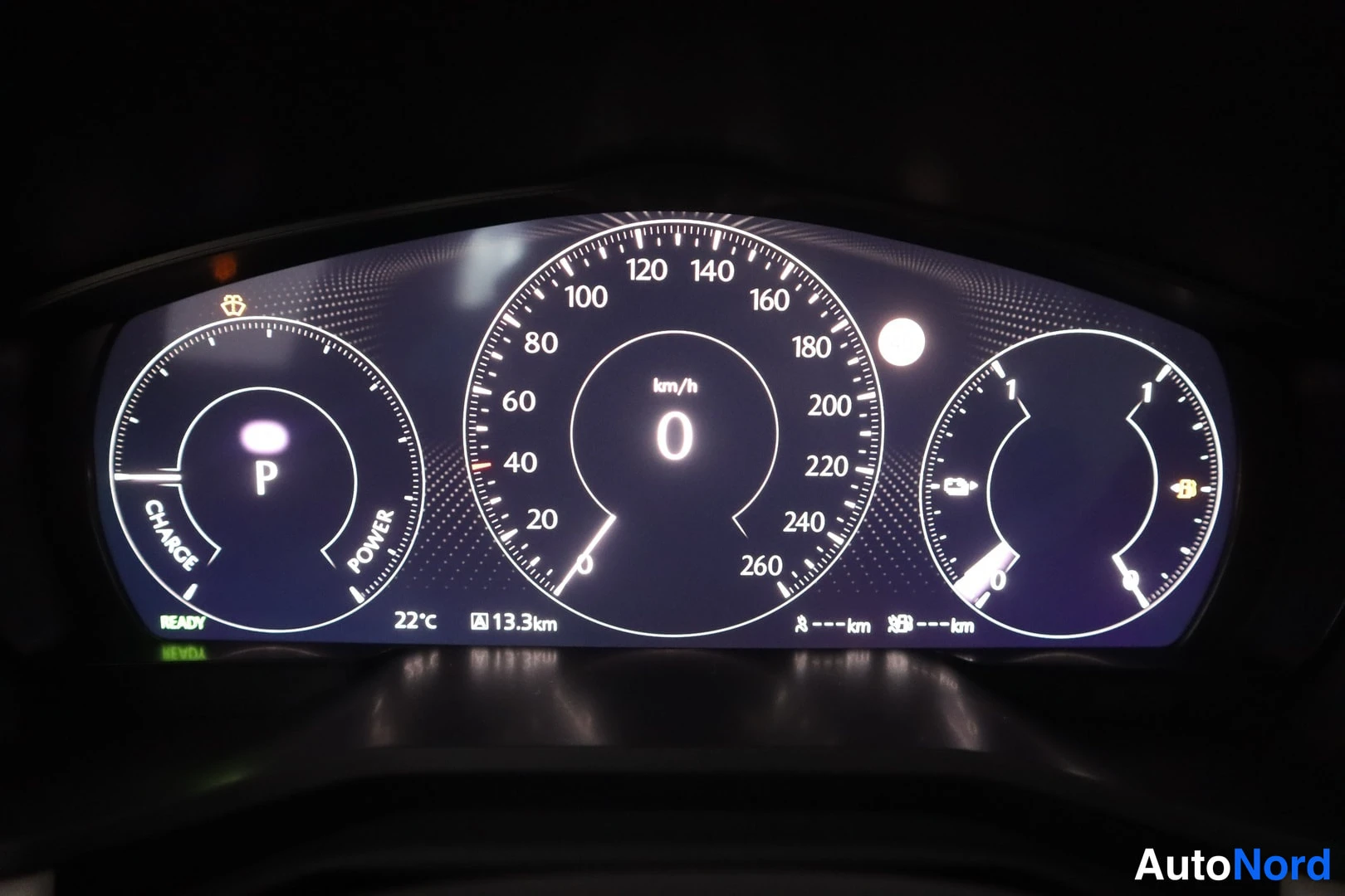Yksityiskohta: Digital instrument cluster display showing speedometer at 0 km/h, power meter indicating CHARGE/POWER modes, and ambient temperature 22°C.