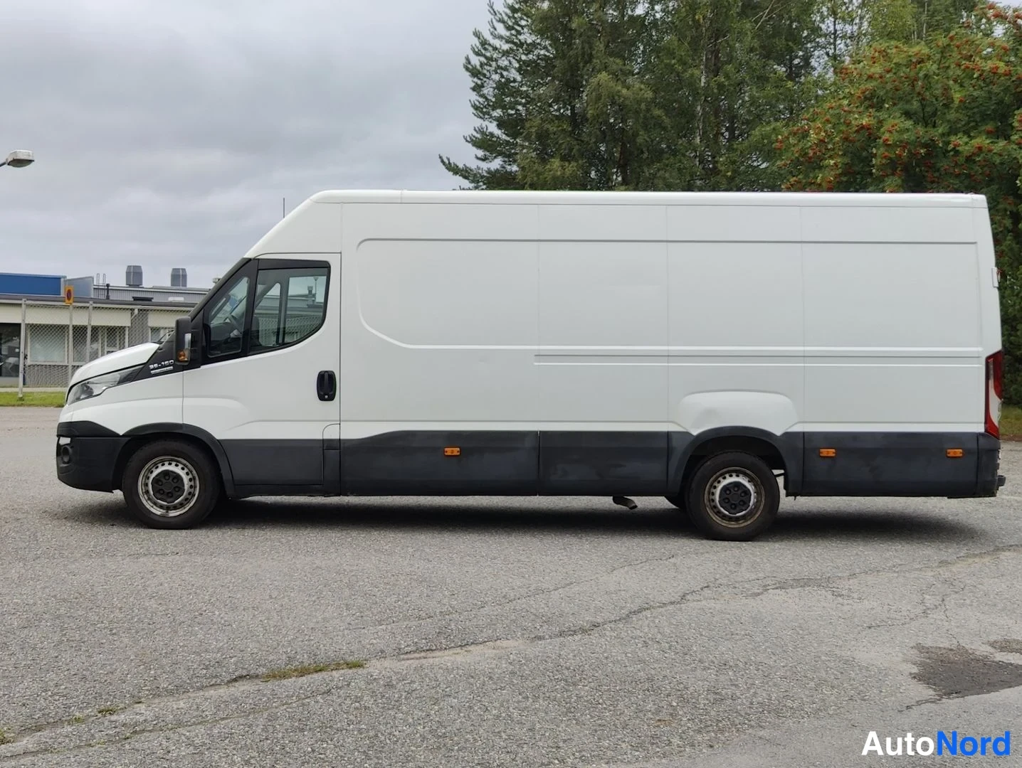 Sivulta: Valkoinen pitkä Iveco Daily -pakettiauto kuvattuna vasemmasta etukulmasta; auton koko kylki ja keula näkyvät, puskurit ja alakolmat tummat.