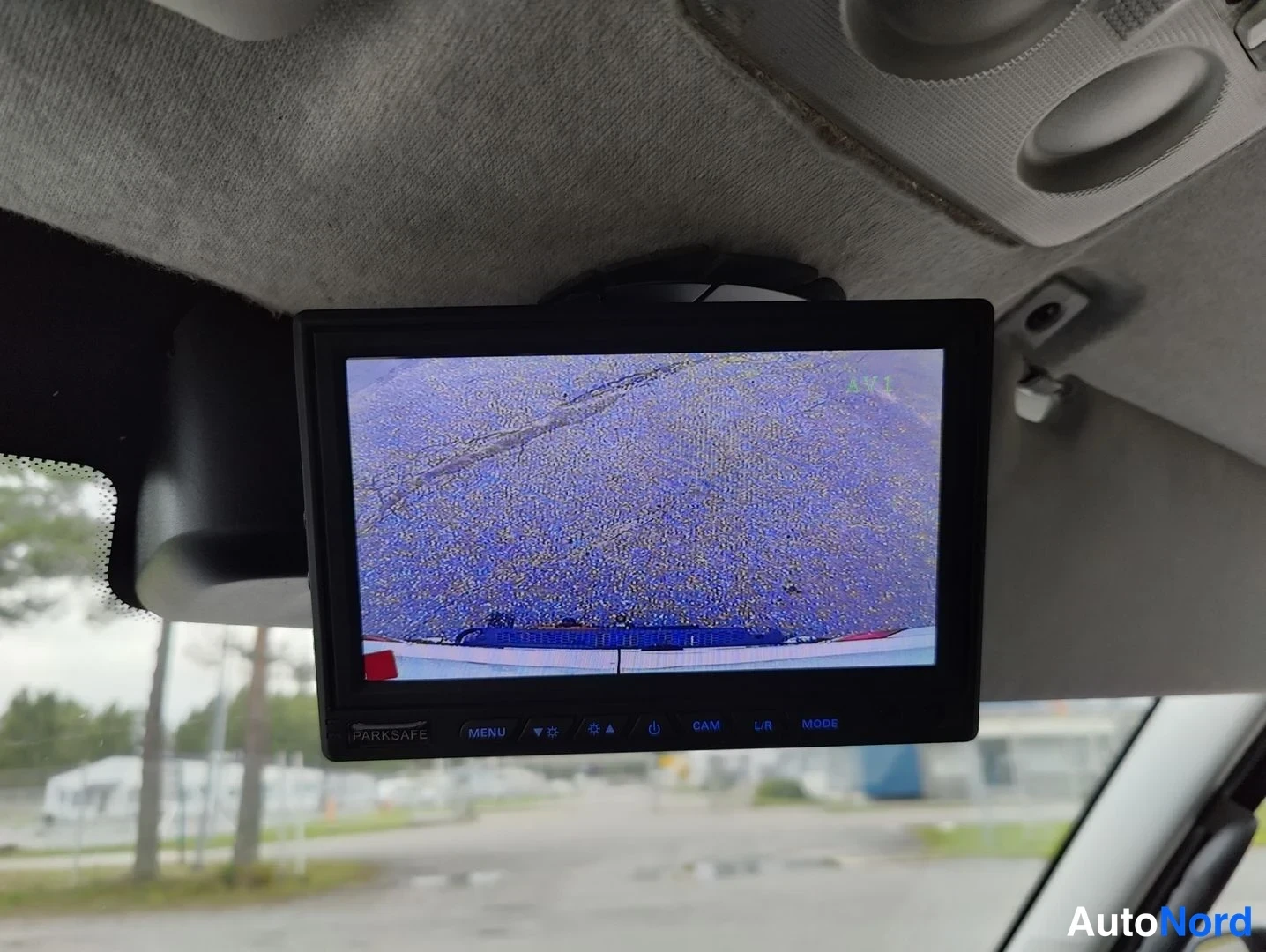 Ohjaamo: Aftermarket reversing camera display mounted on ceiling showing grainy blue-tinted video feed with PARKSAFE branding