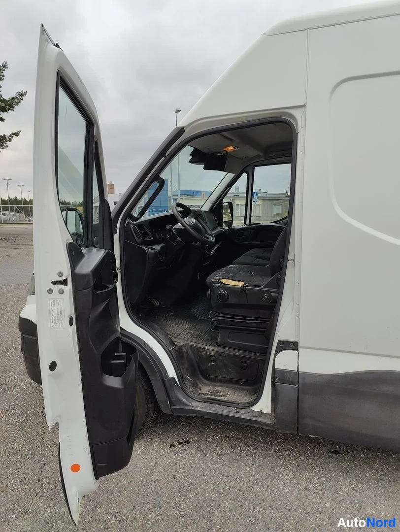 Sivulta: Valkoinen pakettiauto vasemmalla puolella; ovi on auki. Sisällä näkyy ohjaamossa olevat istuimet ja mustat lattiapäälliset.