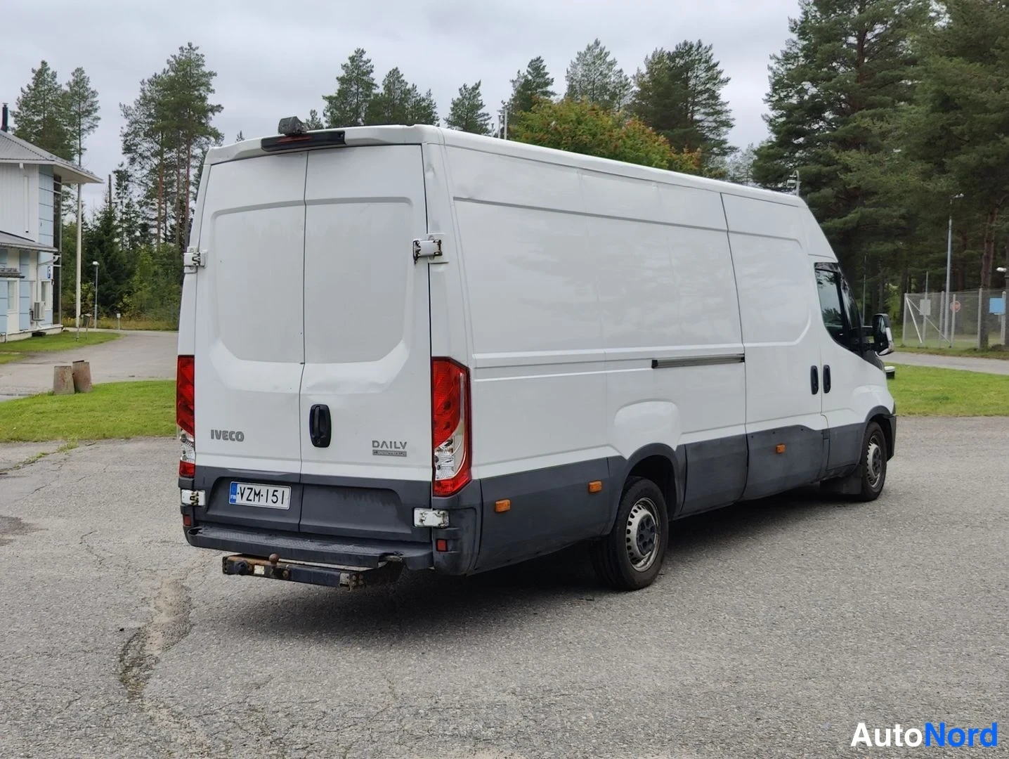 Takaviisto: Valkoinen Iveco Daily -pakettiauto kuvattuna takaviistosta; pystysuorat takavalot, takapaneelissa IVECO- ja DAILY-merkit, rekisterikilpi, pitkät kylkipaneelit j