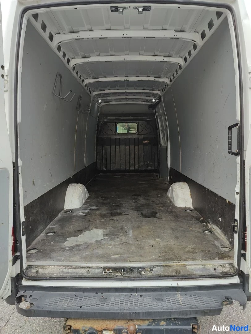 Takaa: Close-up view into empty cargo compartment through fully opened rear doors, black lower wall trim and floor tie-down points visible