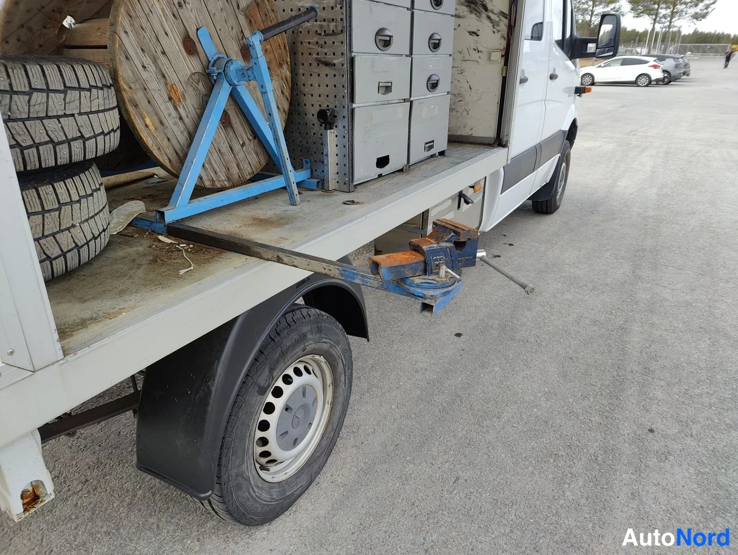 Sivulta: Right flank of a white commercial truck with an open flatbed cargo area. A black mudguard covers the rear wheel which has a steel rim. On the bed are two stacke