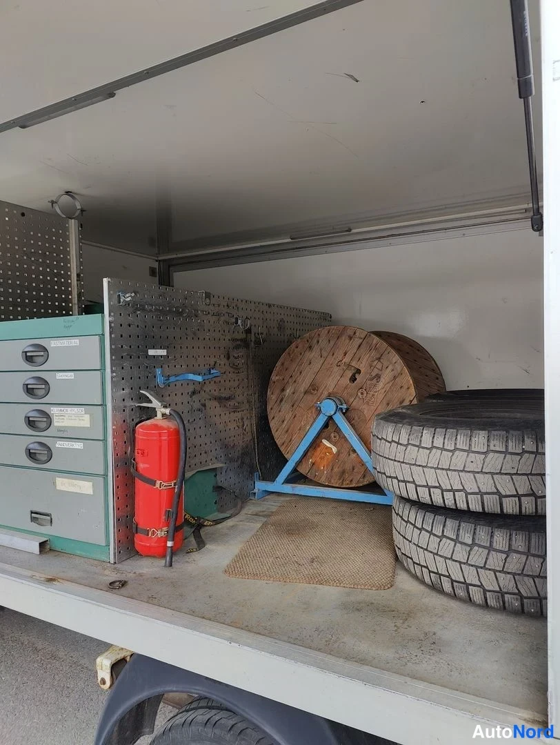 Tavaratila: Interior shot of the truck's cargo box from the side opening. The view shows a white painted interior floor and walls. Visible contents include a stack of four
