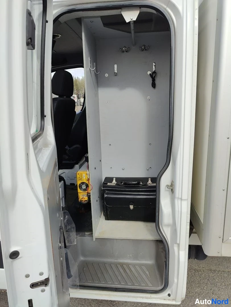Tavaratila: A look into the rear cargo area of a white van with the side door open. The interior features grey paneling on the walls and floor, hooks mounted near the ceili