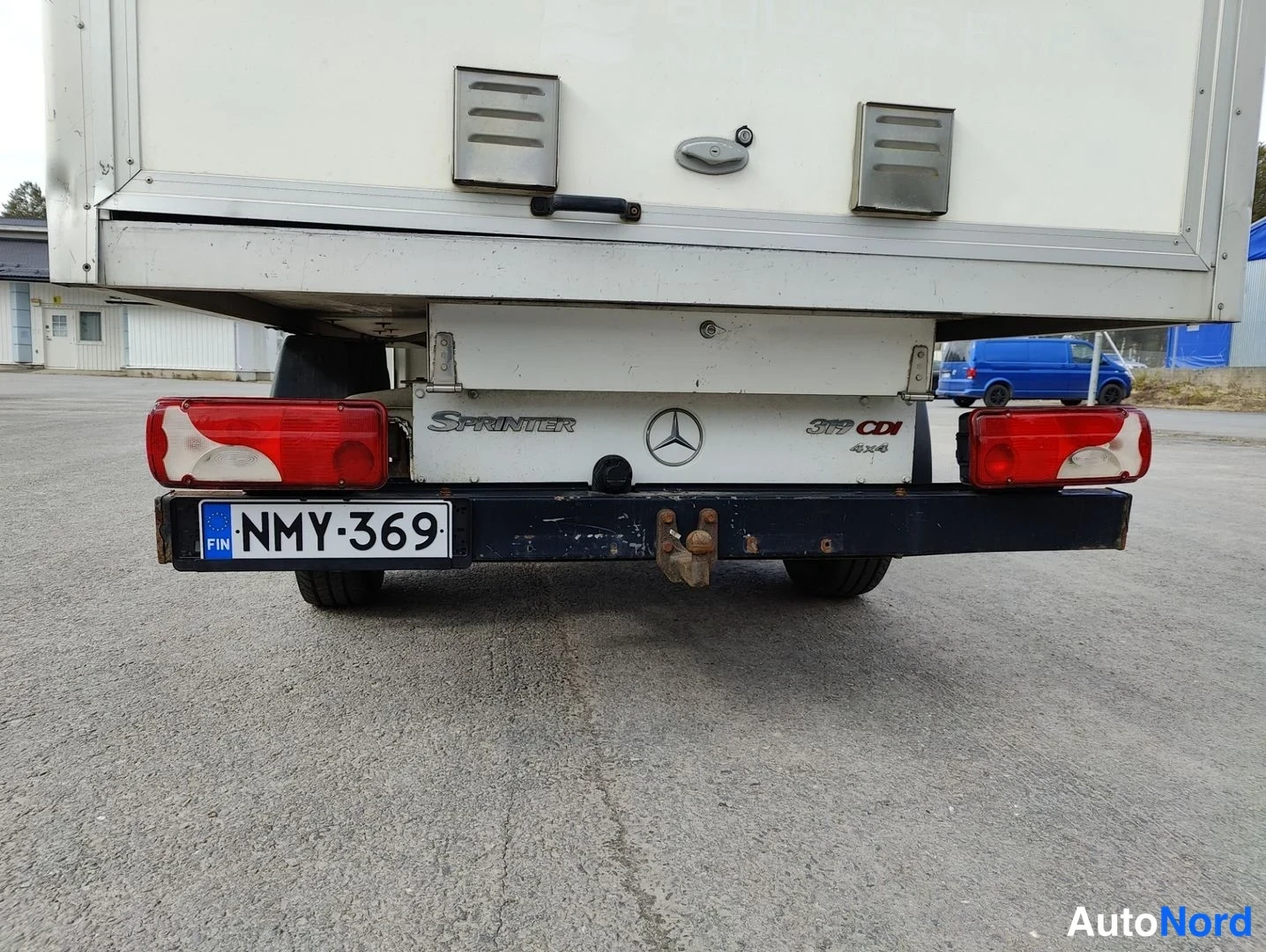 Takaa: Rear view of a white Mercedes-Benz Sprinter 312 CDI with a box body (Erilliskori). A dark blue tow hitch bar shows signs of surface rust. The Finnish license pl