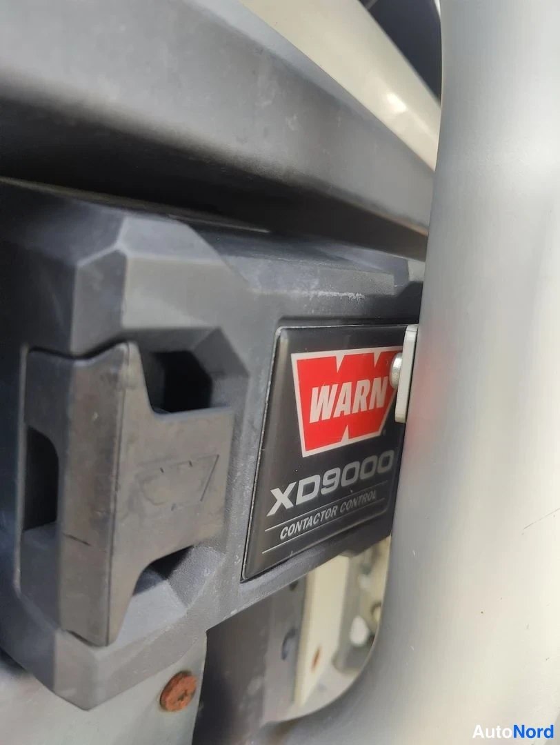 Yksityiskohta: Lähikuva ajoneuvoon asennetusta WARN XD9000 -vinssin kontaktorirasiasta; mustassa kotelossa punainen WARN-logotarra ja teksti CONTACTOR CONTROL.