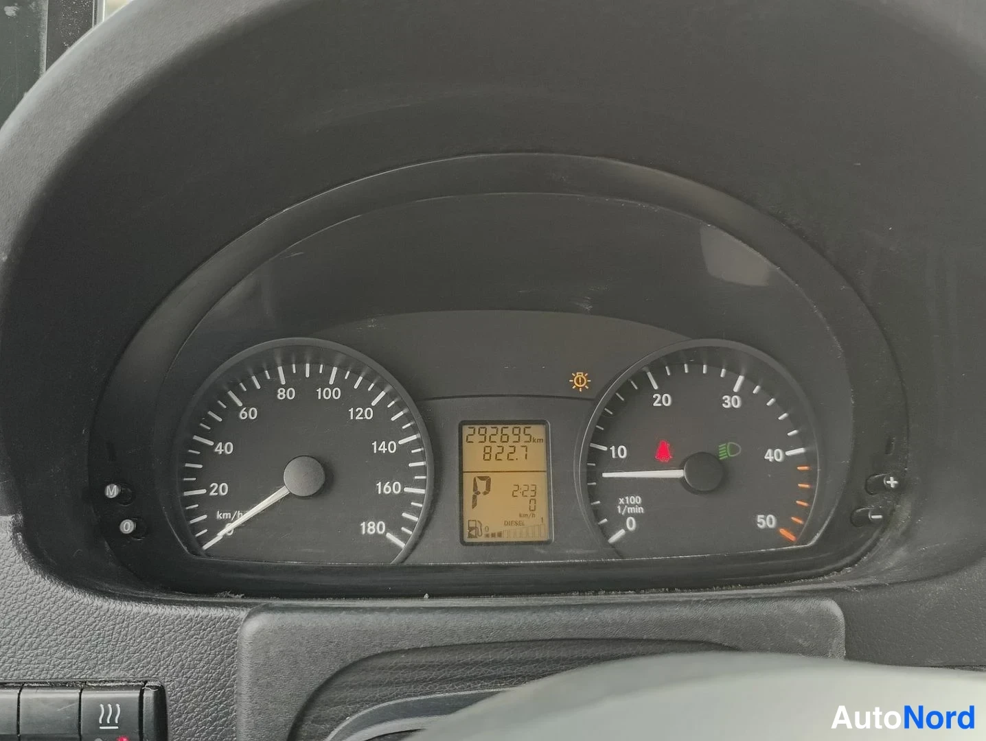 Yksityiskohta: Mittariston lähikuva. Näytössä kuljettomat 292695 km. Kellonajan näyttö ja varoitusvalo päällä.