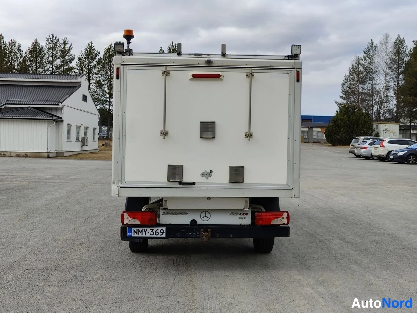Takaa: Takakuvaus valkoisesta Mercedes-Benz Sprinter -alustasta, jossa on erillinen kova kori. Takakontin ovissa on lukitussulku ja punainen takavalojen yläpuolella ol