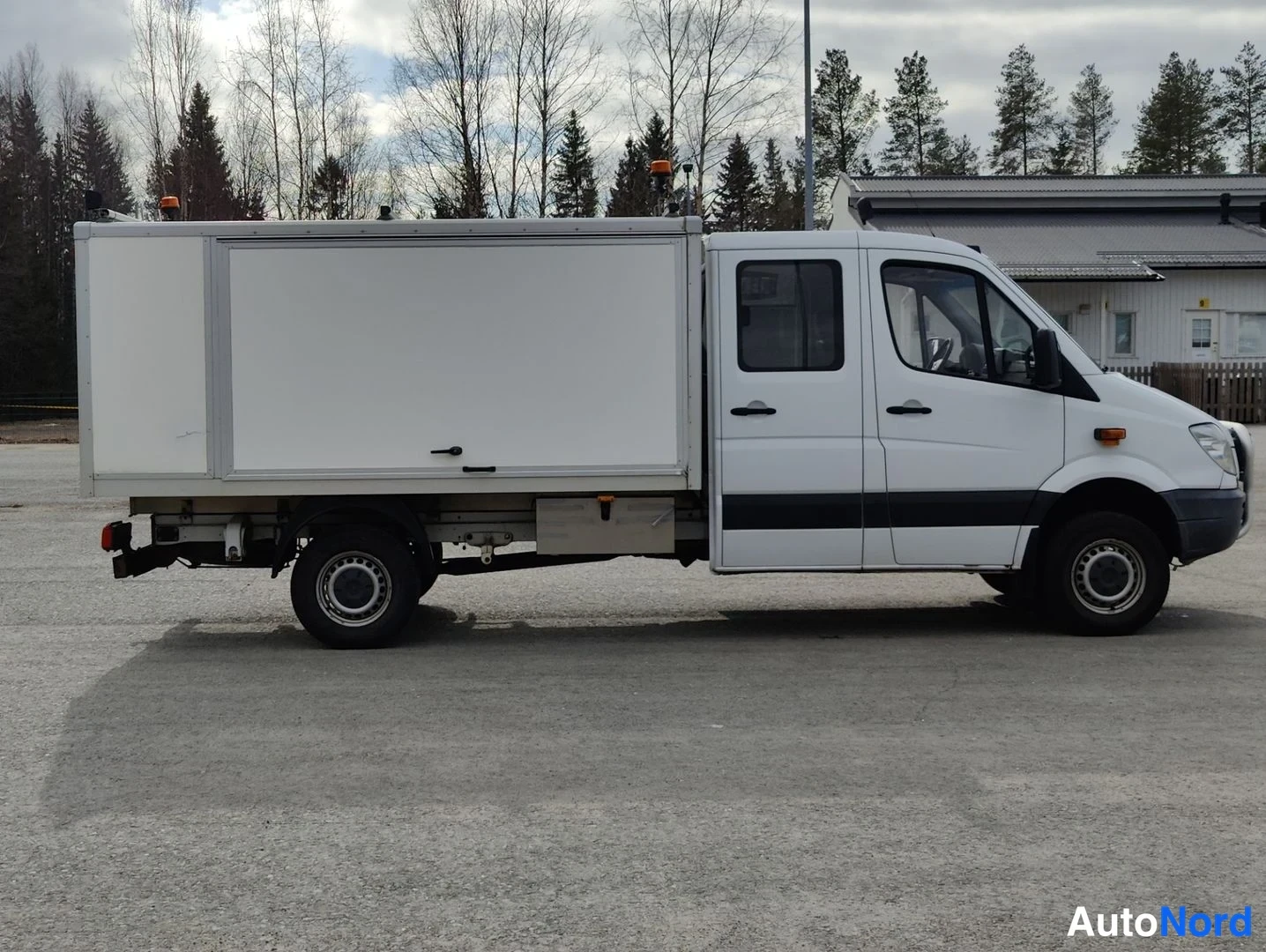 Sivulta: Sivakuva valkoisesta Mercedes-Benz Sprinter -pakettiauto-alustasta, jossa on erillinen kova kori. Auto on neliovinen malli. Sivussa näkyvät alumiinivanteet. Kor