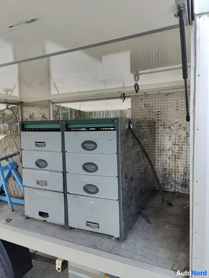 Takaa: Rear view of the cargo area looking in through open rear doors. Two grey filing cabinets are positioned side-by-side. To the far left, part of a blue stand and