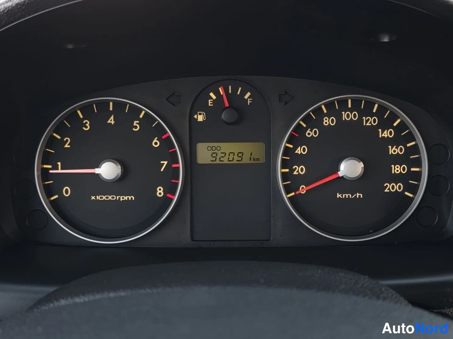 Yksityiskohta: Kojelaudan mittaristo lähikuvassa: kierrosmittari (x1000rpm), nopeusmittari (km/h), polttoainemittari ja digitaalinen ODO-näyttö, joka lukee 92091 km.
