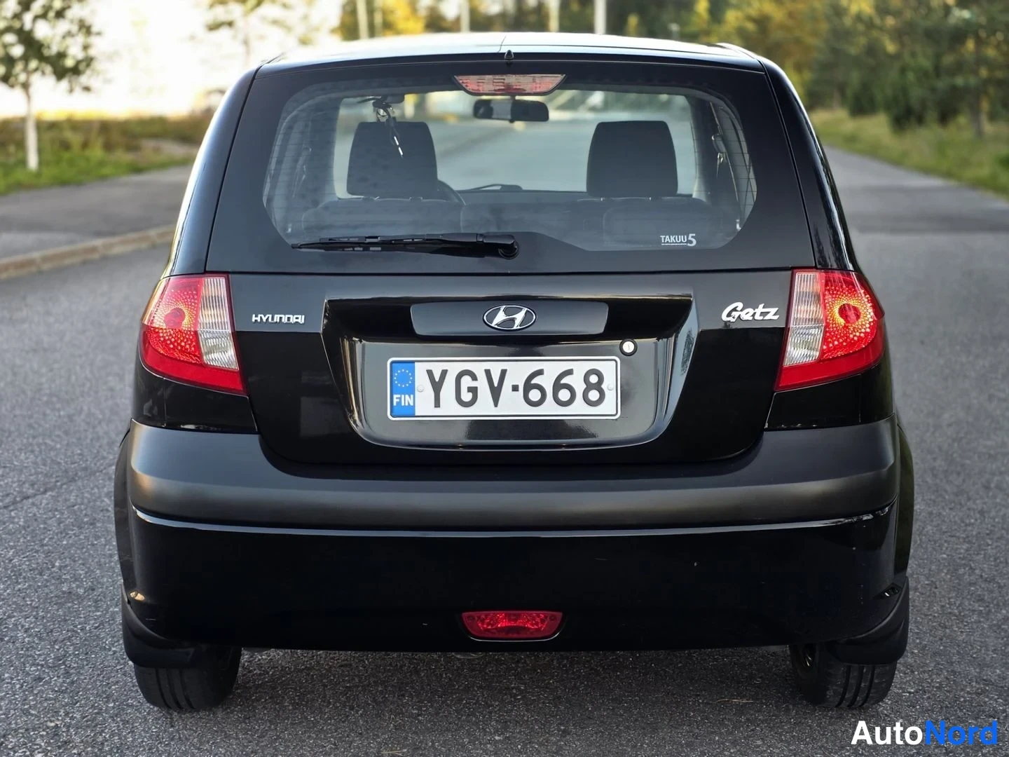 Takaa: Suora takakuva. Mustassa Hyundai Getzissä on taivaltakki ja takakamera (pieni ympyrävalaisin takapuskurissa). Mallimerkki 'Getz', merkki 'Hyundai' sekä rekister