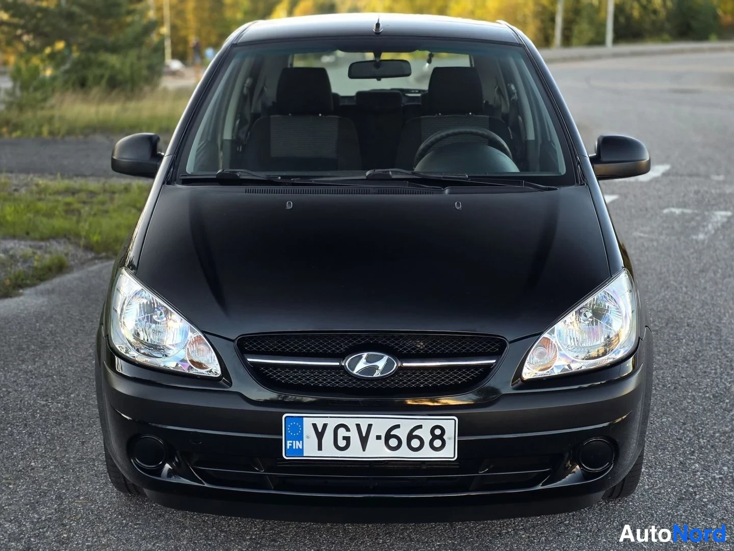 Edestä: Kuva ajoneuvosta etupuolelta, jossa näkyy auton etuosan rakenne, including grille and headlights. Kuvassa näkyy myös osittain etuistuimet ja ohjaamon sisusta.