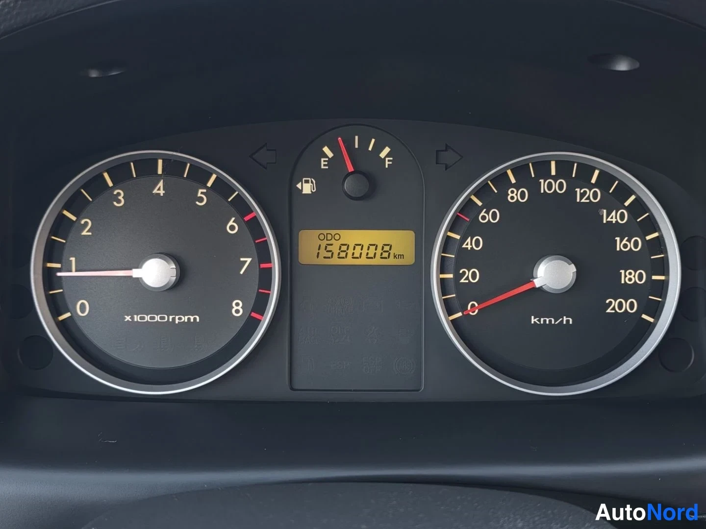 Yksityiskohta: Mittariston lähikuva: nopeusmittari (km/h) ja kierroslukumittari (x1000rpm), polttoainemittari sekä ODO-näyttö, jossa lukee 158008 km.