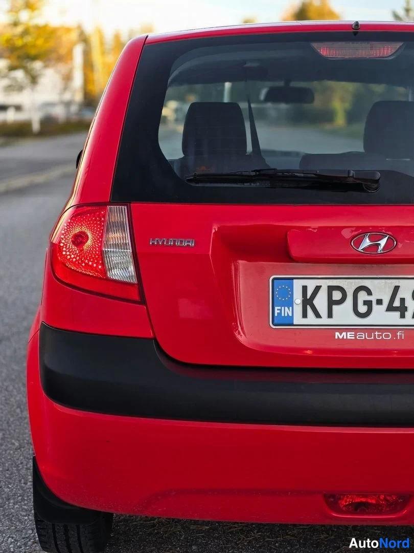 Takaa: Punaisen Hyundai-hatchbackin takanäkymä: HYUNDAI-teksti ja logon merkintä takaluukussa, takavalasto vasemmalla, takaikkunassa pyyhkijä, rekisterikilpi alkaa mer