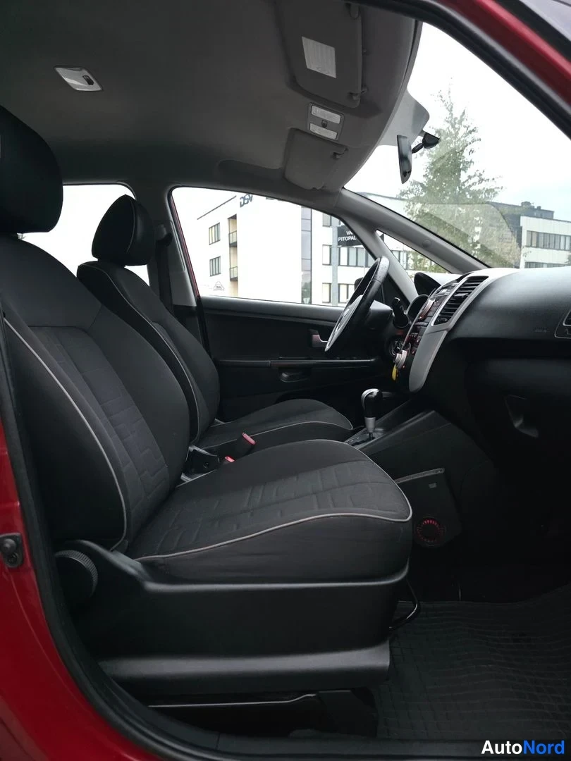 Etuistuimet: Front cabin with two black fabric front seats, steering wheel to the left and dashboard extending to the right. Centre console between seats.