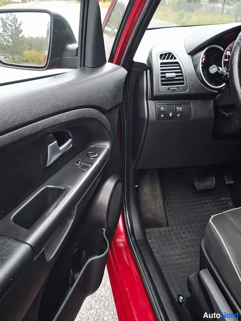 Ohjaamo: Driver's door panel showing window switch cluster, door handle, storage pocket, and speaker grille next to the red exterior door jamb.