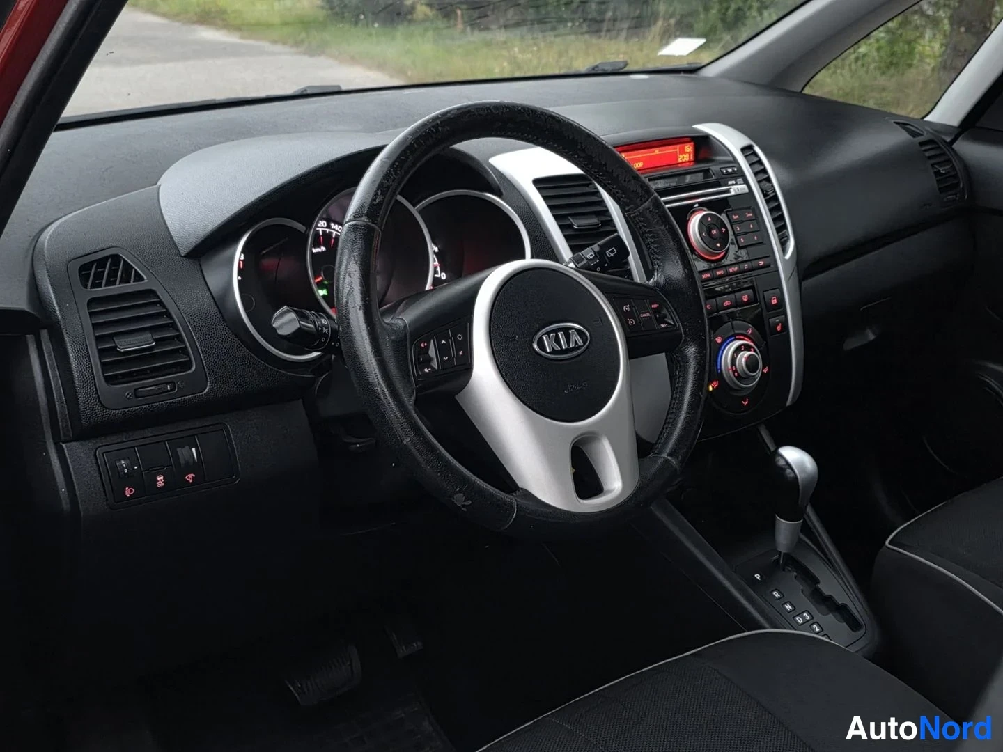 Ohjaamo: Interior view focused on the left side of the dashboard and steering wheel, showing air vents, a rotary dial behind the steering wheel, and buttons for front/re