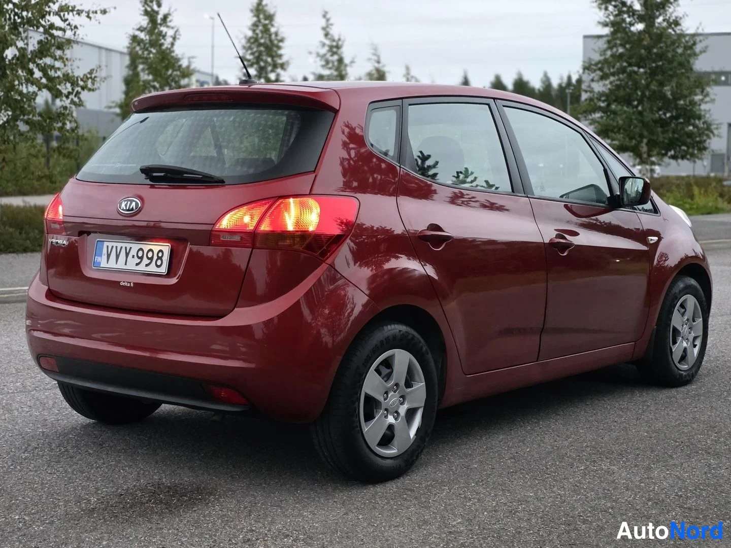 Takaviisto: Rekisterikilpi ja takavaloilla varustettu punainen Kia Venga -henkilöauto takasivusta.