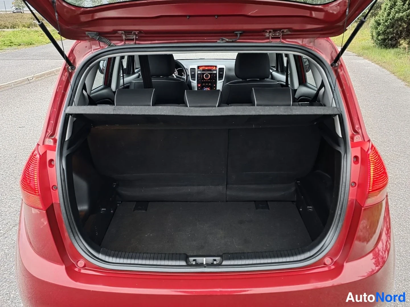 Tavaratila: Red vehicle boot with hatch open. A cargo divider is across the boot opening. The rear seats are visible beyond the divider.