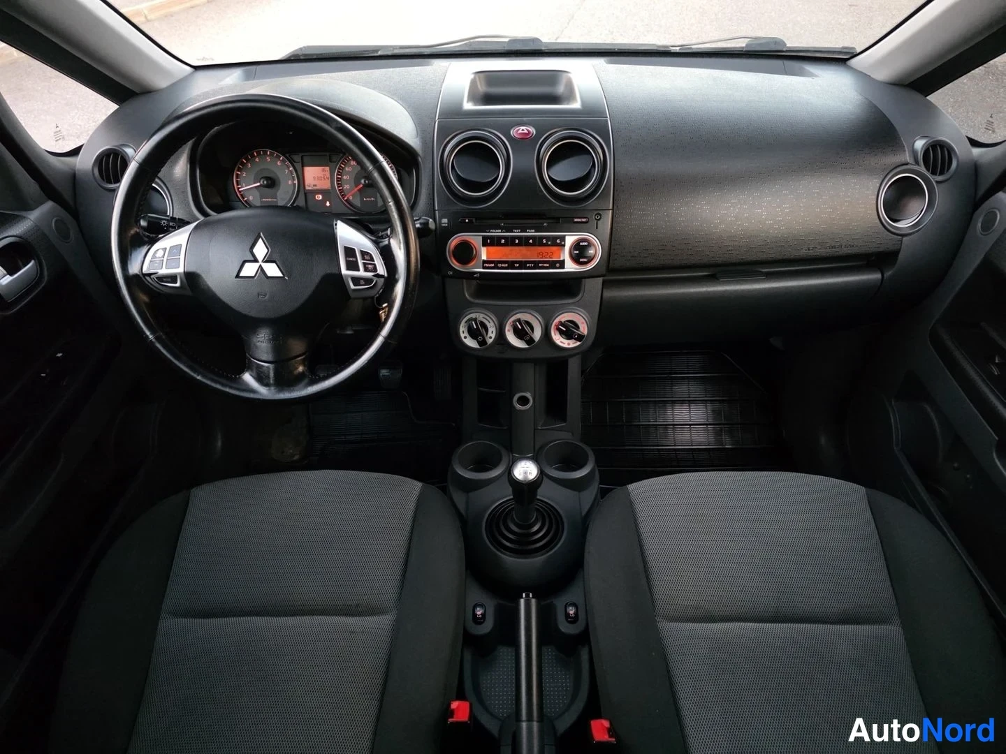 Etuistuimet: Interiörbild från främre sätet som visar styrhjul med Mitsubishi-logotyp, instrumentpanel, manuell växelspake och mörkgrå tygstolar.