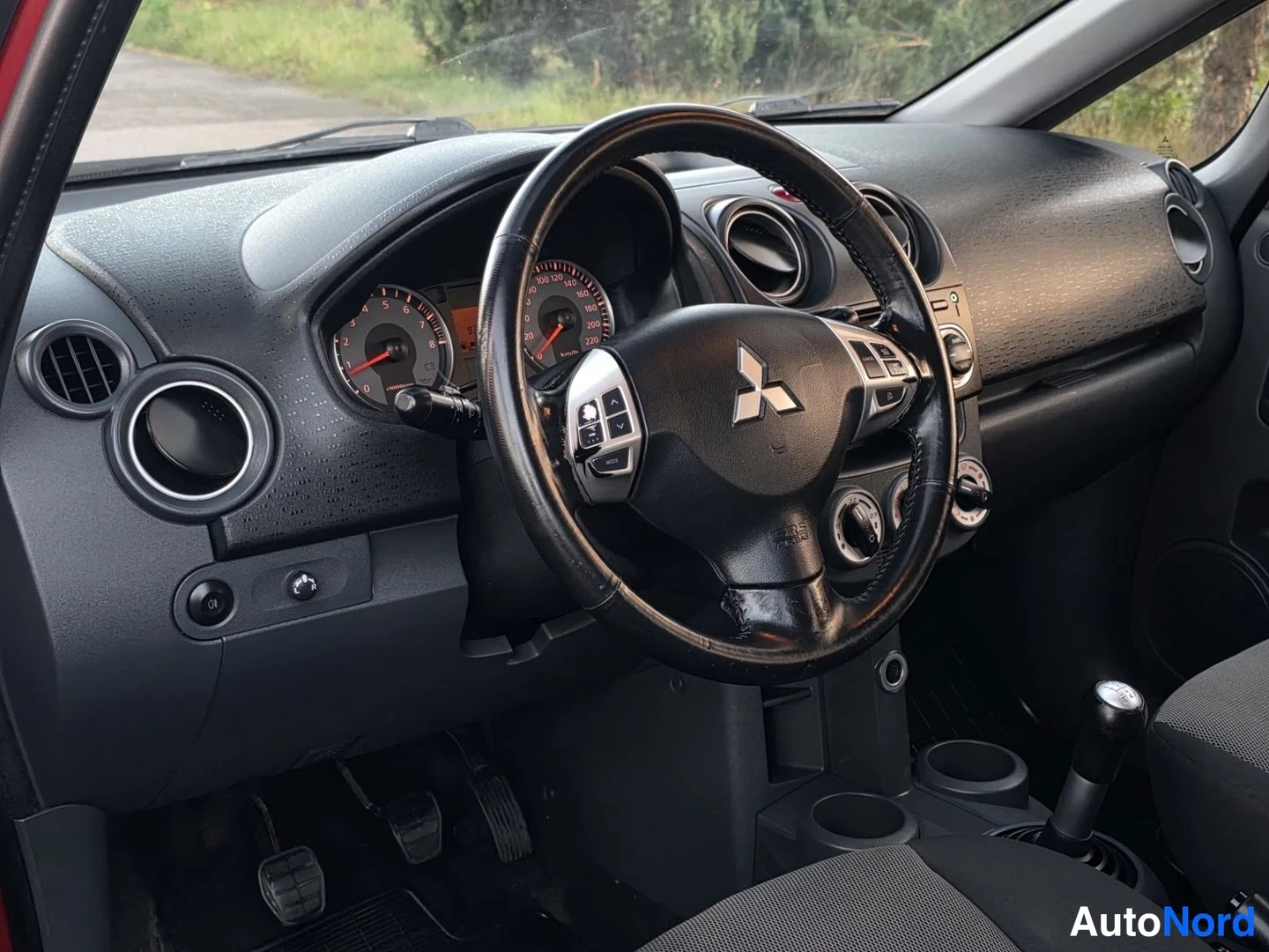 Etuistuimet: Vinkel på förarsidan som visar styrhjul, instrumentpanel med turer och mätare, spakar för motorfunktioner under ratten och trappor för fotpedaler.