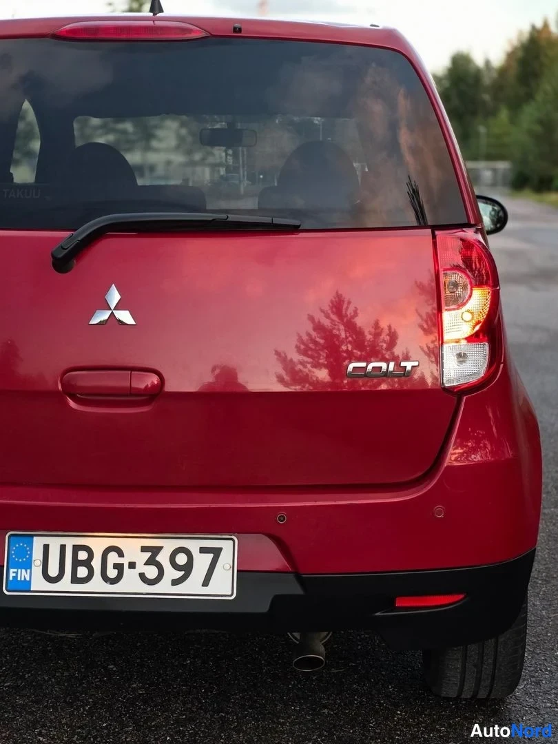 Takaa: Auto takaa nähtynä: punainen Mitsubishi Colt -pakettiova. Kaksi valoa oikealla, takaluukun 'COLT' merkintä. Luku. Ilmoitus ikkunassa: 'AITO 5 VUODEN TAKUU'.