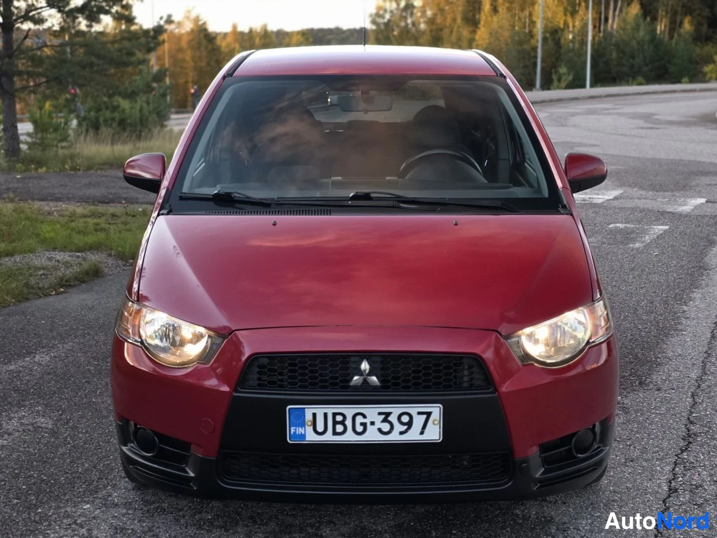 Edestä: Mitsubishi Colt suoraan edestä nähtynä. Punainen etupää, including grilli ja katsojat.