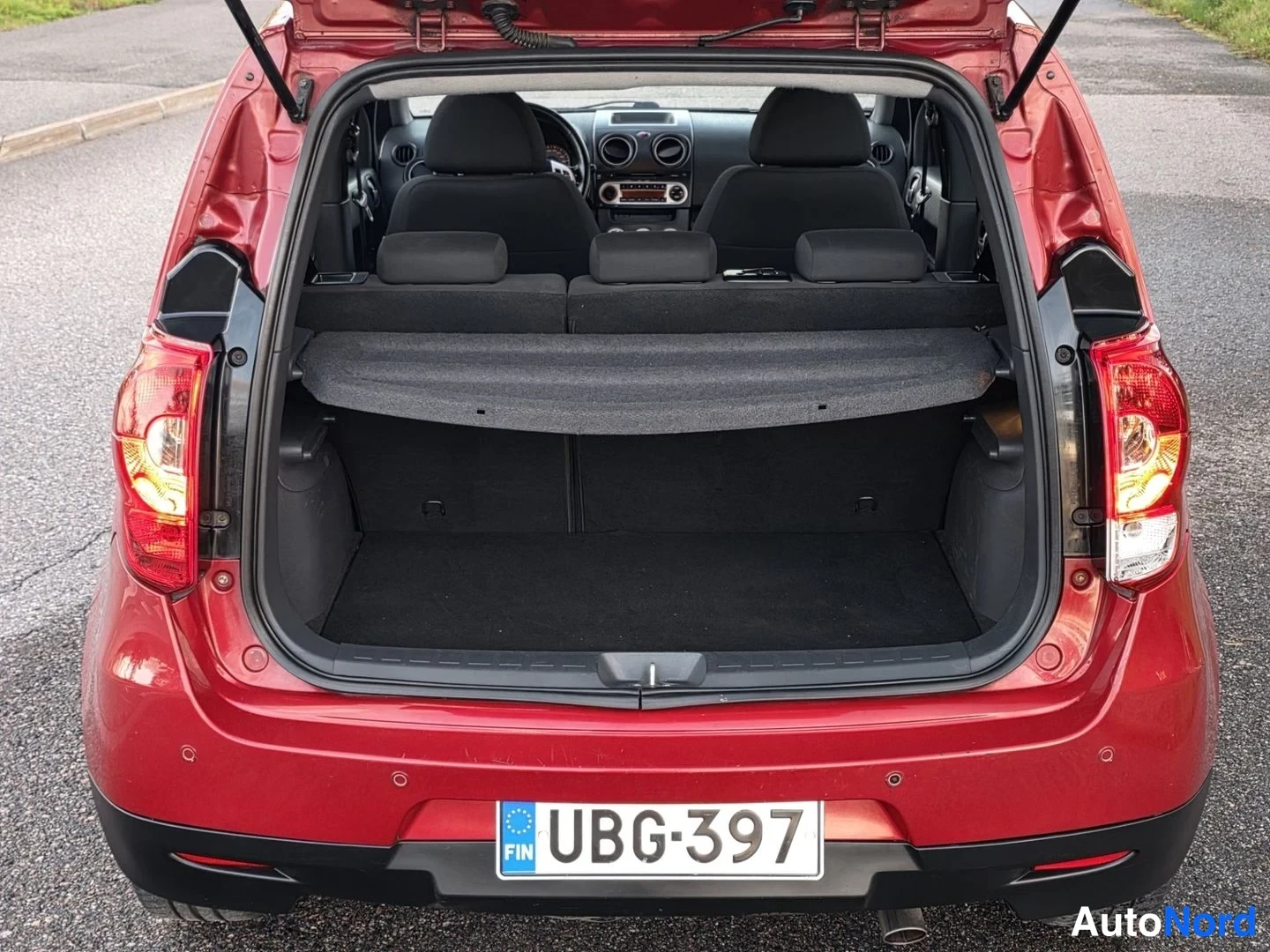 Takaa: Rear view of a red hatchback with the tailgate open revealing the trunk area and rear seats through the opening