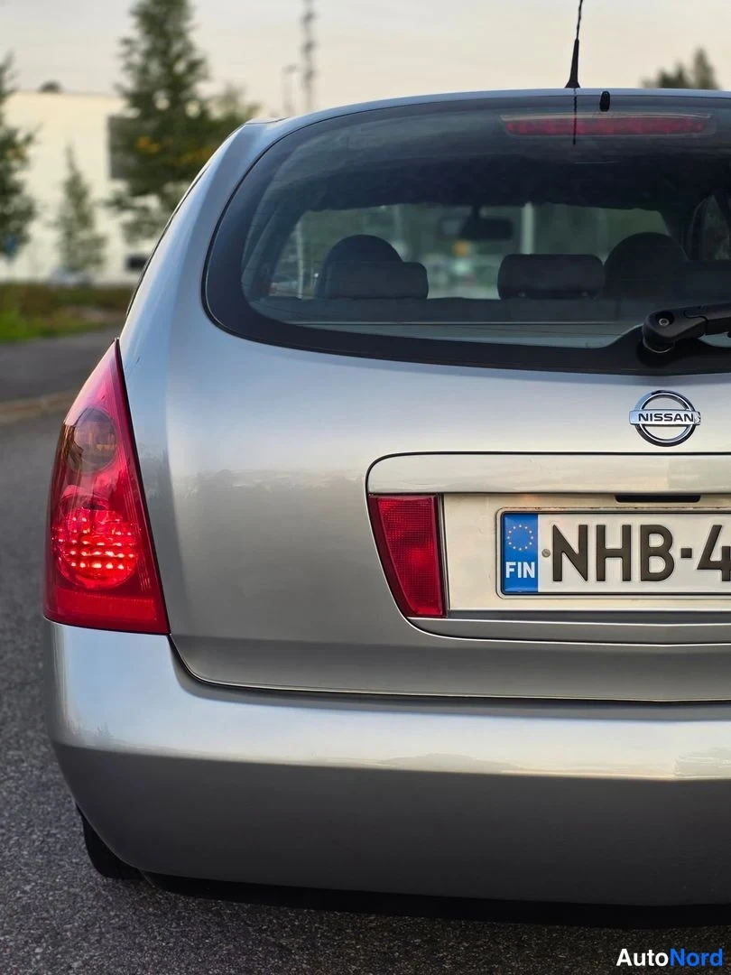 Takaa: Auton takapään lähikuva: hopeanvärinen takaluukku, Nissan-merkki, punaiset takavalot ja rekisterikilven alku.