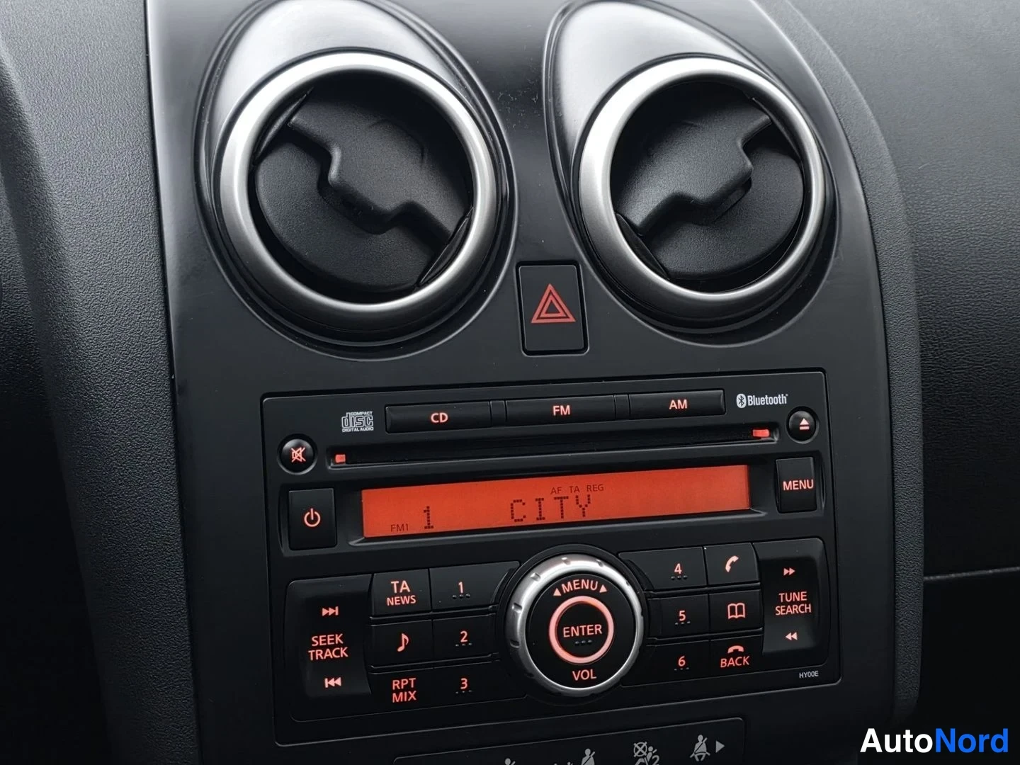 Muu: Keskikonsolin yläosan lähikuva: kaksi pyöreää ilmastointisuutinta ja autoradio-ohjauspaneeli jossa on Bluetooth-logo ja näytön teksti 'CITY'.