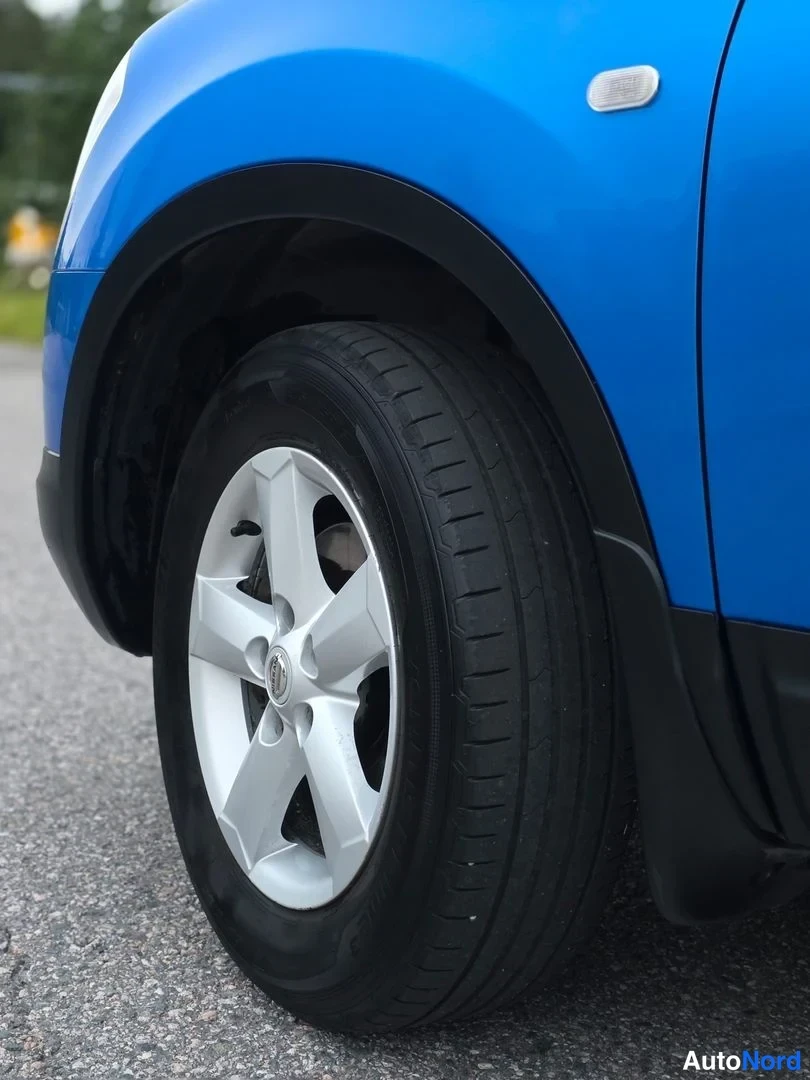 Yksityiskohta: Blue car's front wheel with silver alloy rim and black tyre against asphalt.