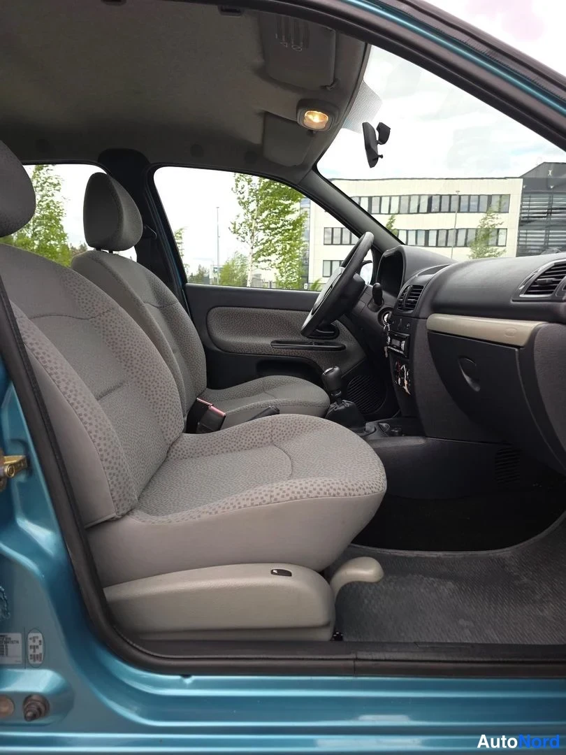 Etuistuimet: Ovetön kuva autosta sisältäpäin etupenkiltä. Vasemmalla puolella on ohjaamossa seisova ohjauspyörä, joka on musta. Ohjaamo on tummansävyinen ja keskivaiheella o