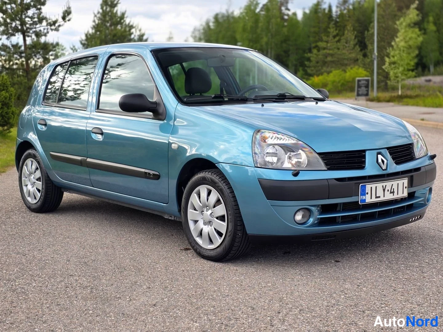 Etuviisto, nokka oikealle: Front three-quarter view of a light blue Renault Clio five-door hatchback showing front and left side with alloy wheels.