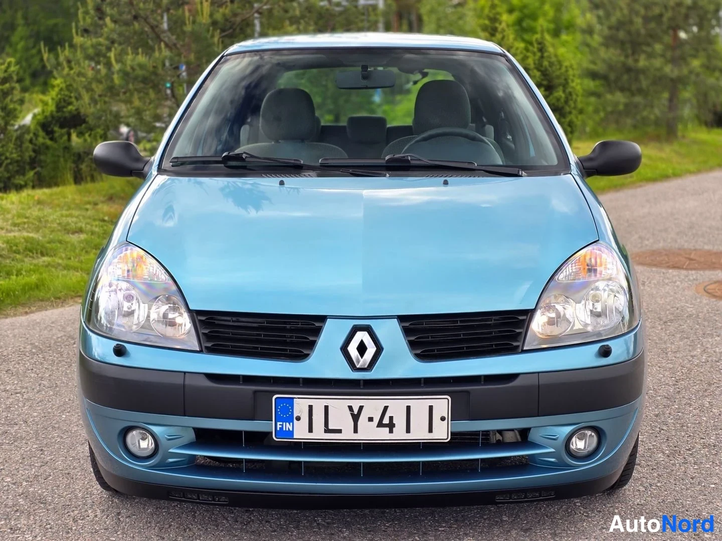 Edestä: Direct front view of a light blue Renault Clio showing grille, headlights, front bumper and licence plate.