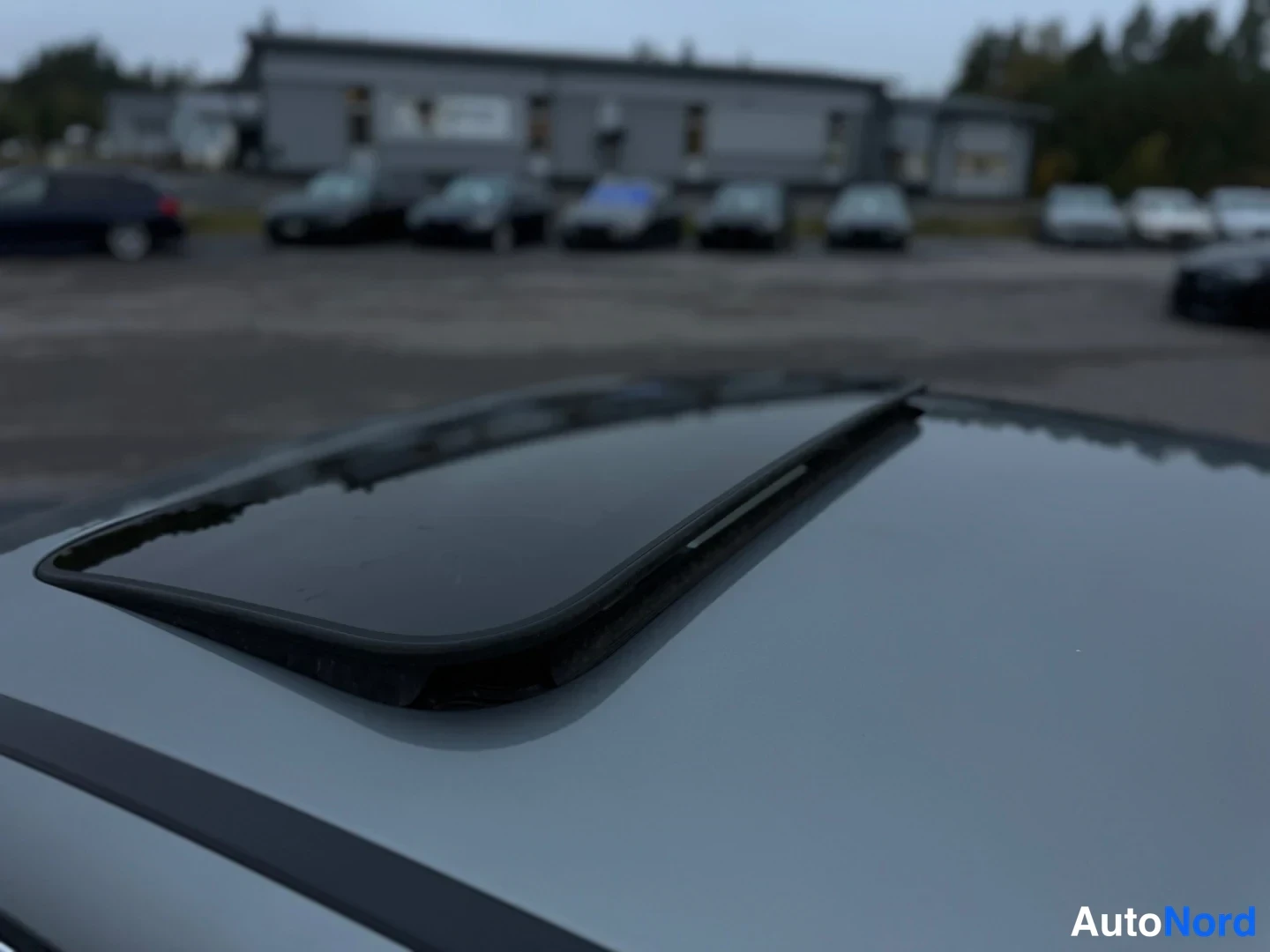Muu: Lähikuva suljetusta aurinkokatosta, jonka lasipinta heijastaa ympäristöä. Katto on hopeanvärisessä autossa.