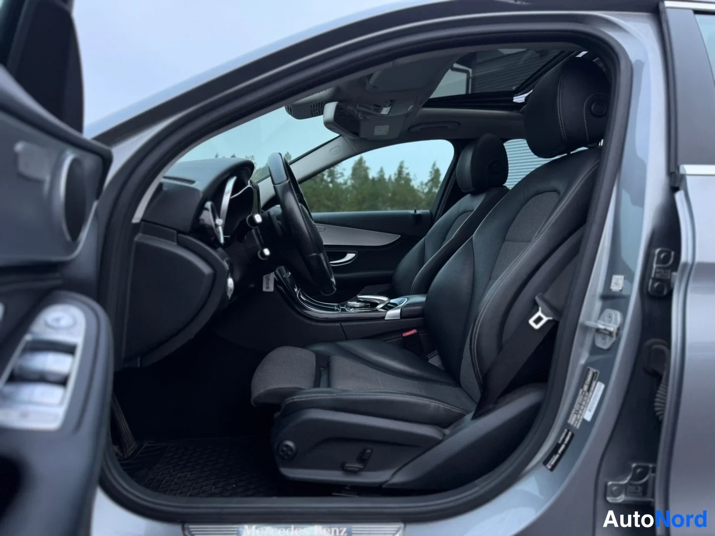 Etuistuimet: Open driver's door view showing two black front bucket seats, steering wheel and dashboard.