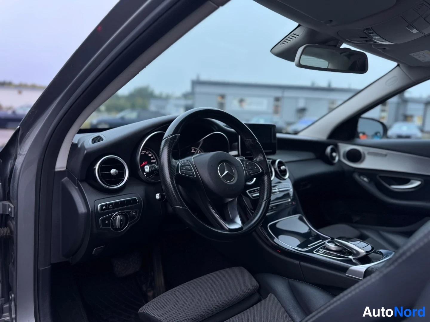 Ohjaamo: Interior view of steering wheel with control buttons, circular air vents and centre console display screen.