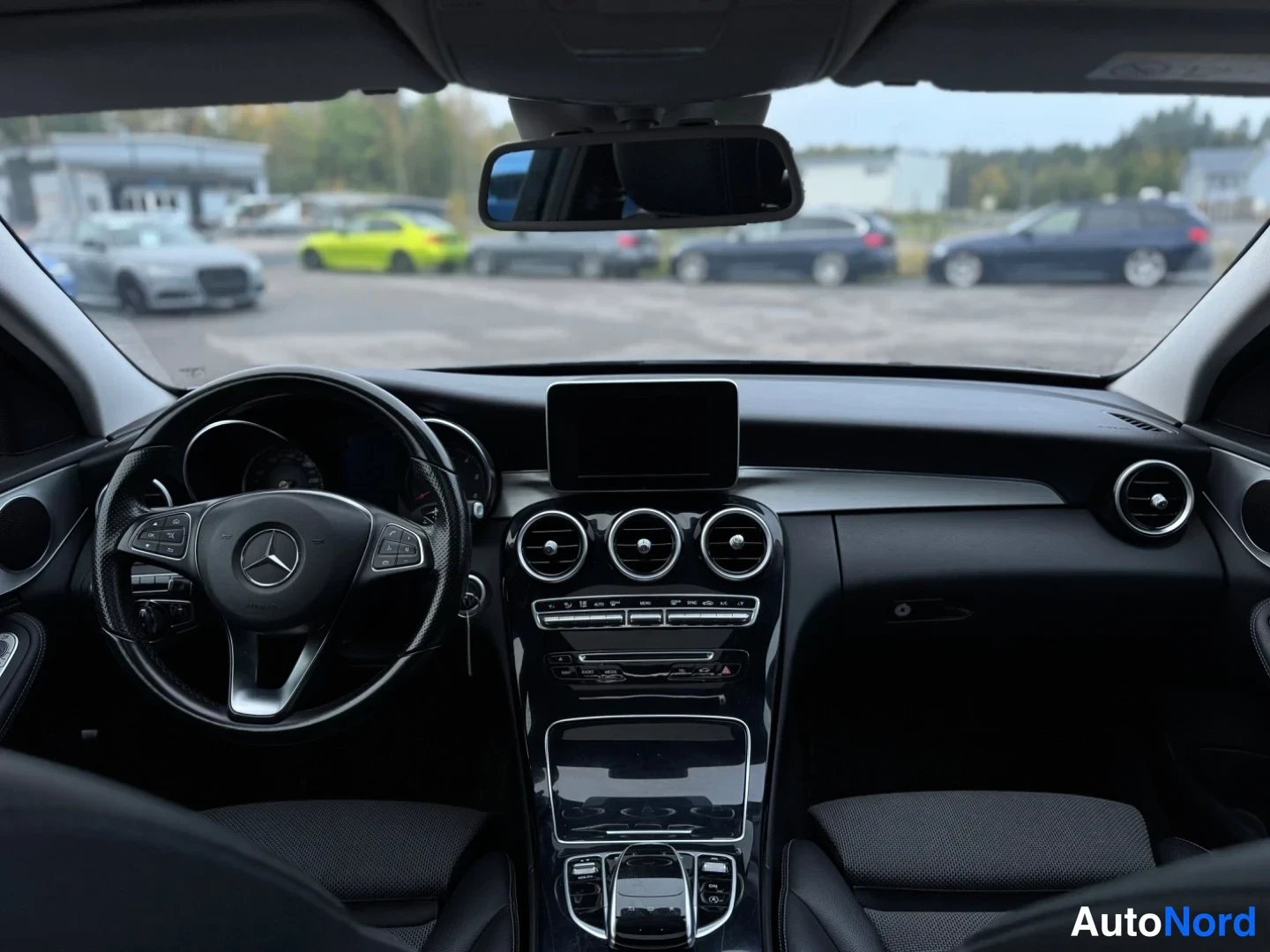 Etuviisto, nokka vasemmalle: Näkymä tuulilasin läpi auton ohjaamosta: Mercedes-merkkinen ratti, keskellä näyttö ja pyöreät suuttimet.