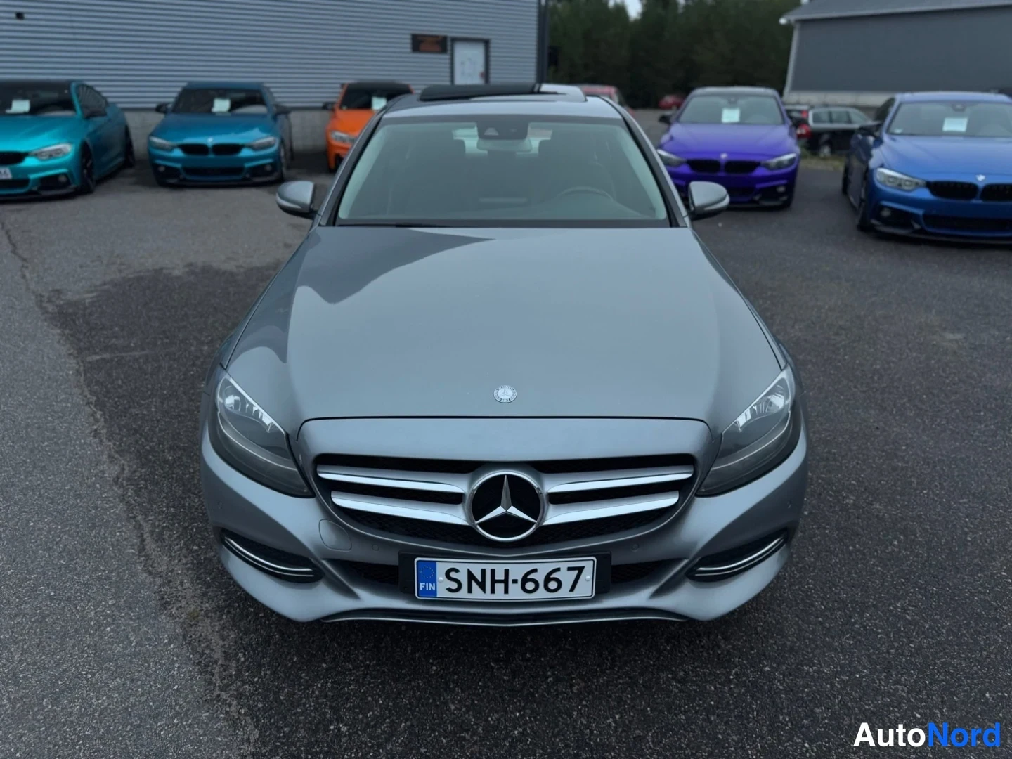 Edestä: Harmaan Mercedes-Benz C -sedanin keula suoraan edestä, Mercedestähti jäähdyttingrillissä, rekisterikilpi.