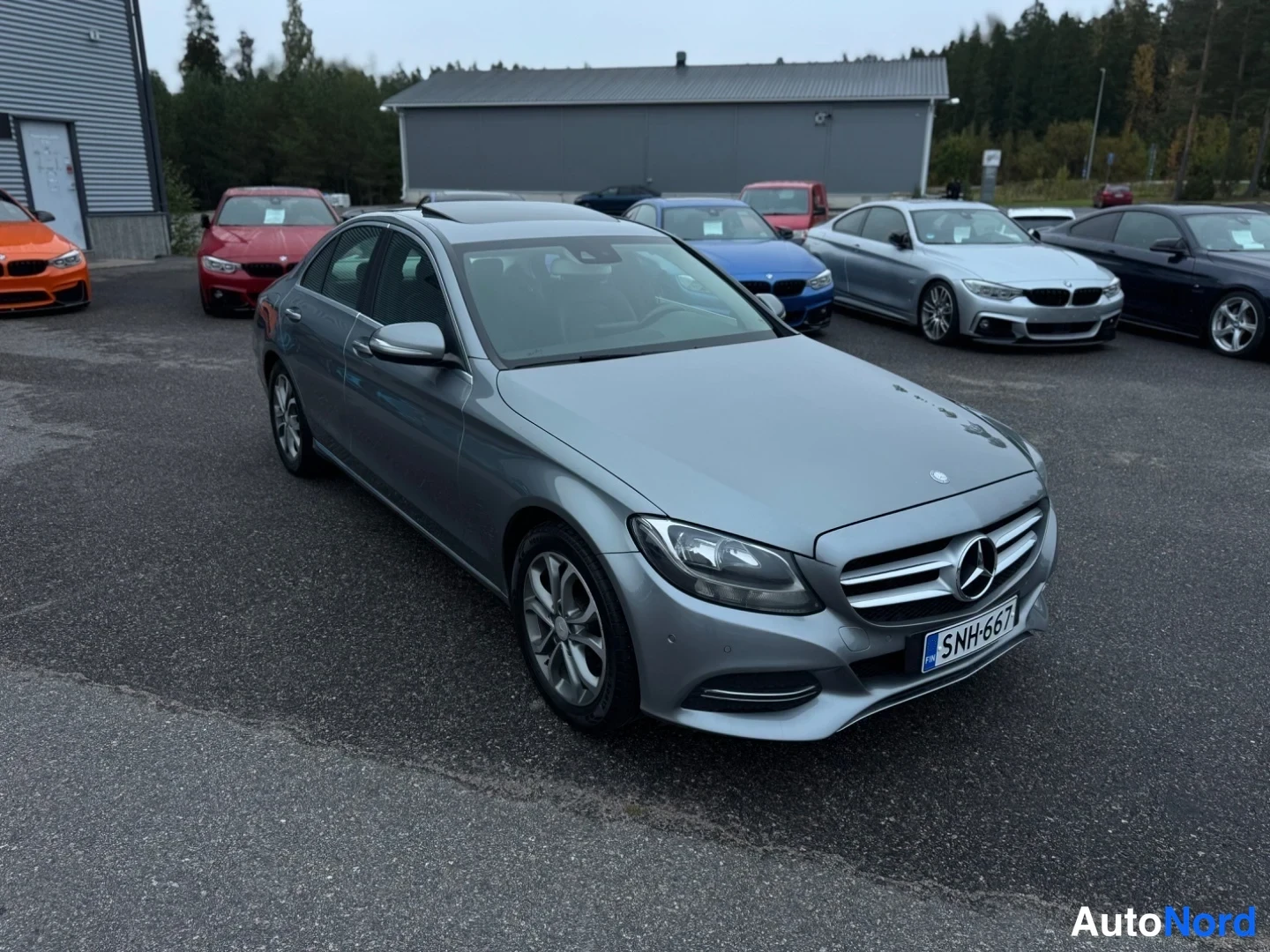 Etuviisto, nokka oikealle: Etukulmasta kuvattu harmaanharmaa Mercedes-Benz-sedan; keula kuvan oikealla, etusäleikkö, ajovalo ja kylki näkyvissä, rekisteritunnus.