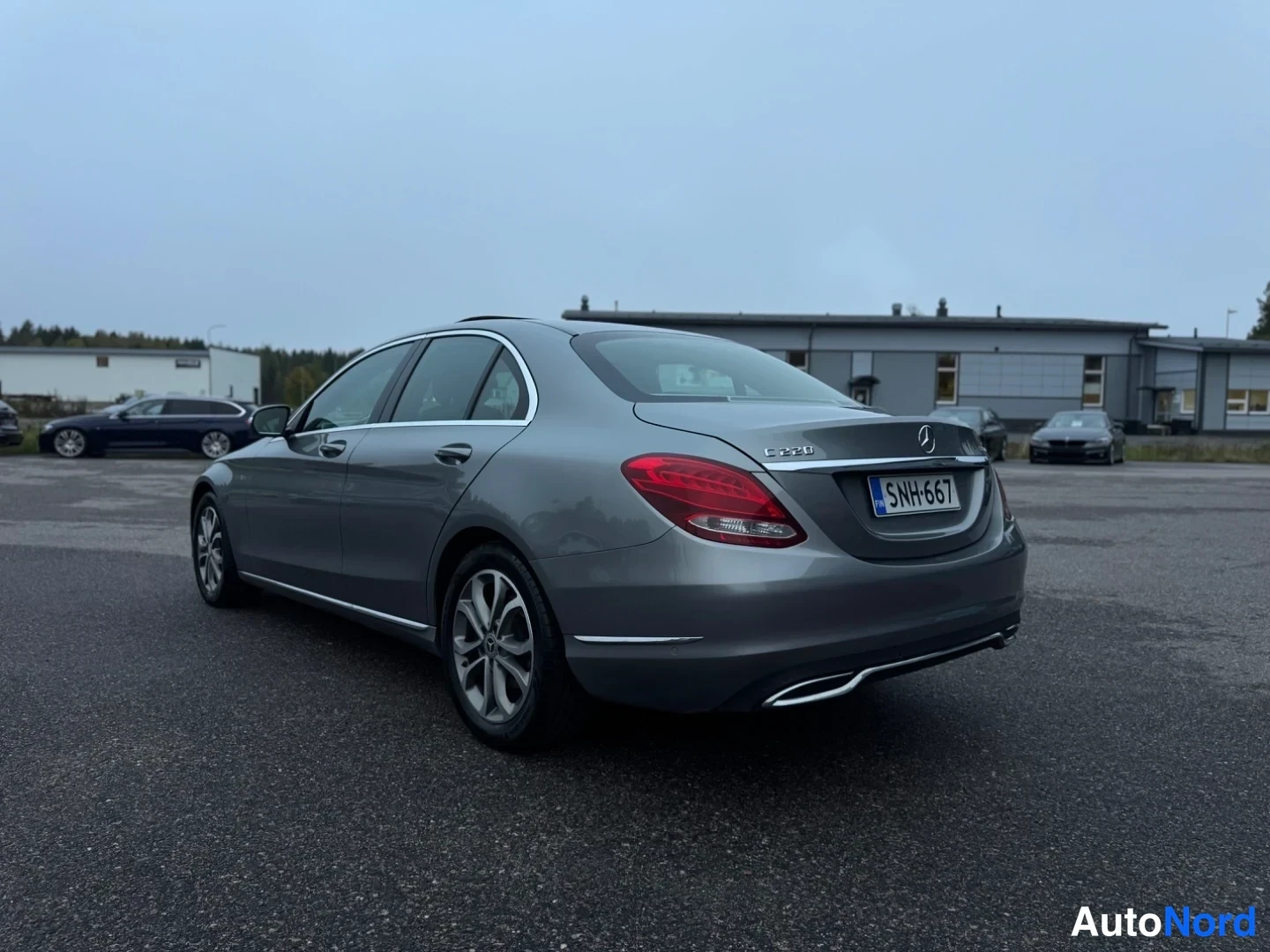 Takaviisto: Takakulmasta kuvattu harmaanharmaa Mercedes-Benz-sedan; takavalot, peräluukku ja kylki näkyvissä, rekisteritunnus.