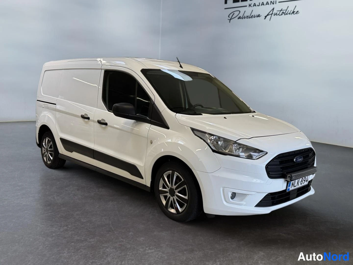 Etuviisto, nokka oikealle: Valkoinen Ford Transit Connect -pakettiauto studio-alueella kolmen neljänneksen kulmasta etuosa näkyvissä.