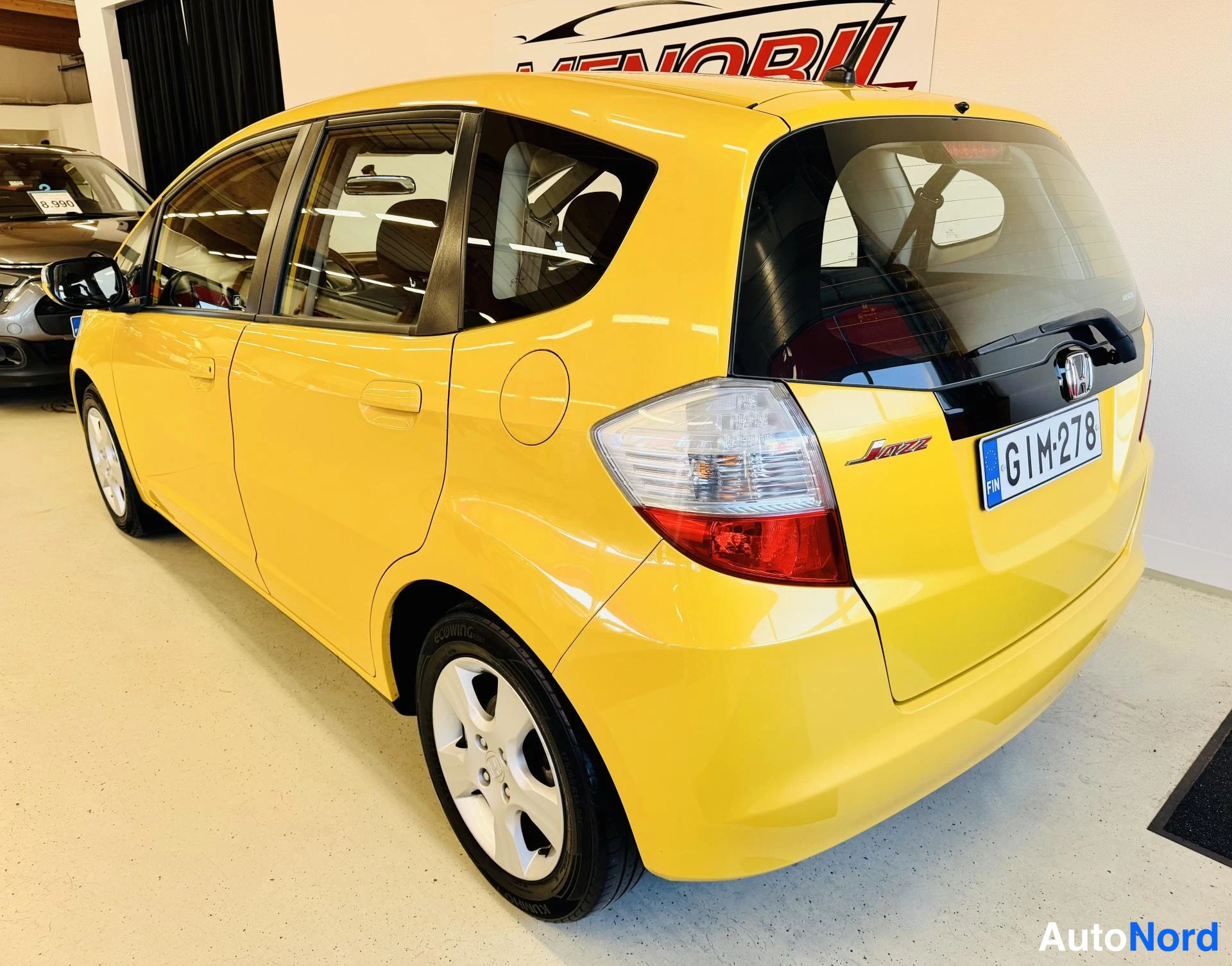 Takaviisto: Keltainen viisiovinen Honda takaa viistosti oikealta kuvattuna, takavalo, JAZZ-merkki ja rekisterikilpi näkyvät.