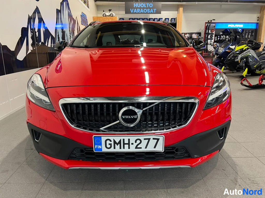 Edestä: Volvo V40 Cross Country etupäästä, punainen kori, Volvo-merkki säleikkössä, rekisterikilpi, auto myyntihallissa.
