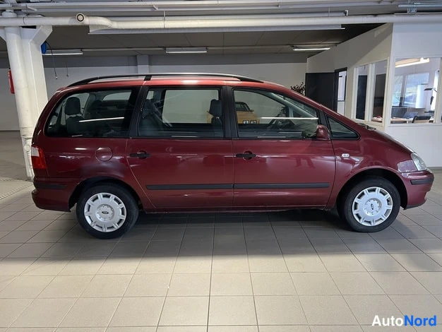 Sivulta: Punaruskea tila-auto sivulta oikealta, kattotelineet ja peräosassa sininen taustapeili, autosalon lattialla.