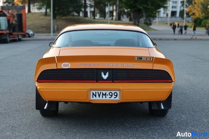 Takaa: Oranssin auton suora takanäkymä; takaosassa teksti TURBO TRANS AM ja rekisterikilpi.