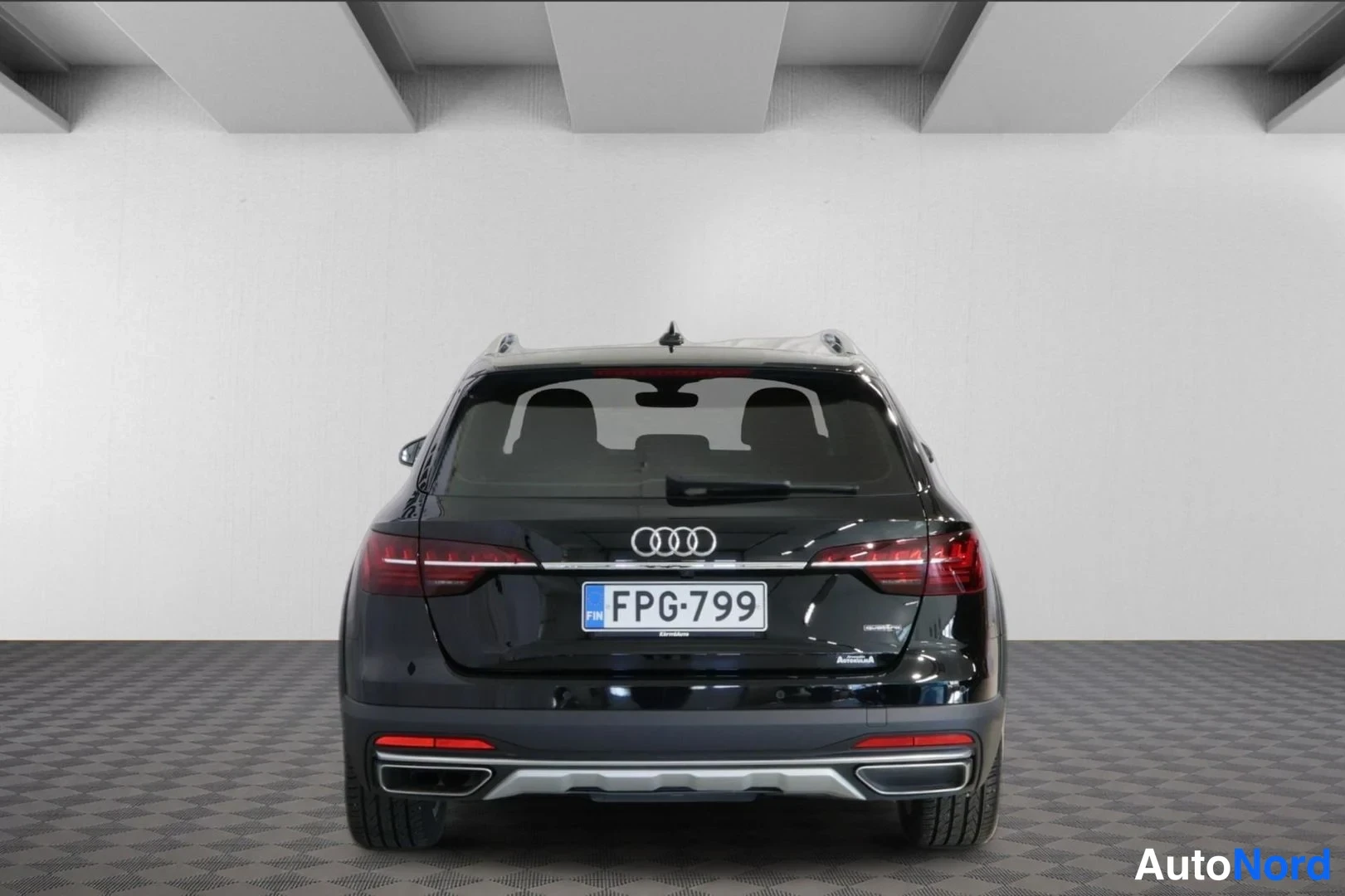 Takaa: Mustan Audi A4 Allroadin takanäkö studiovaloisassa tilassa, rekisterikilpi, kattokaiteet ja kaksoispakoputket näkyvissä.