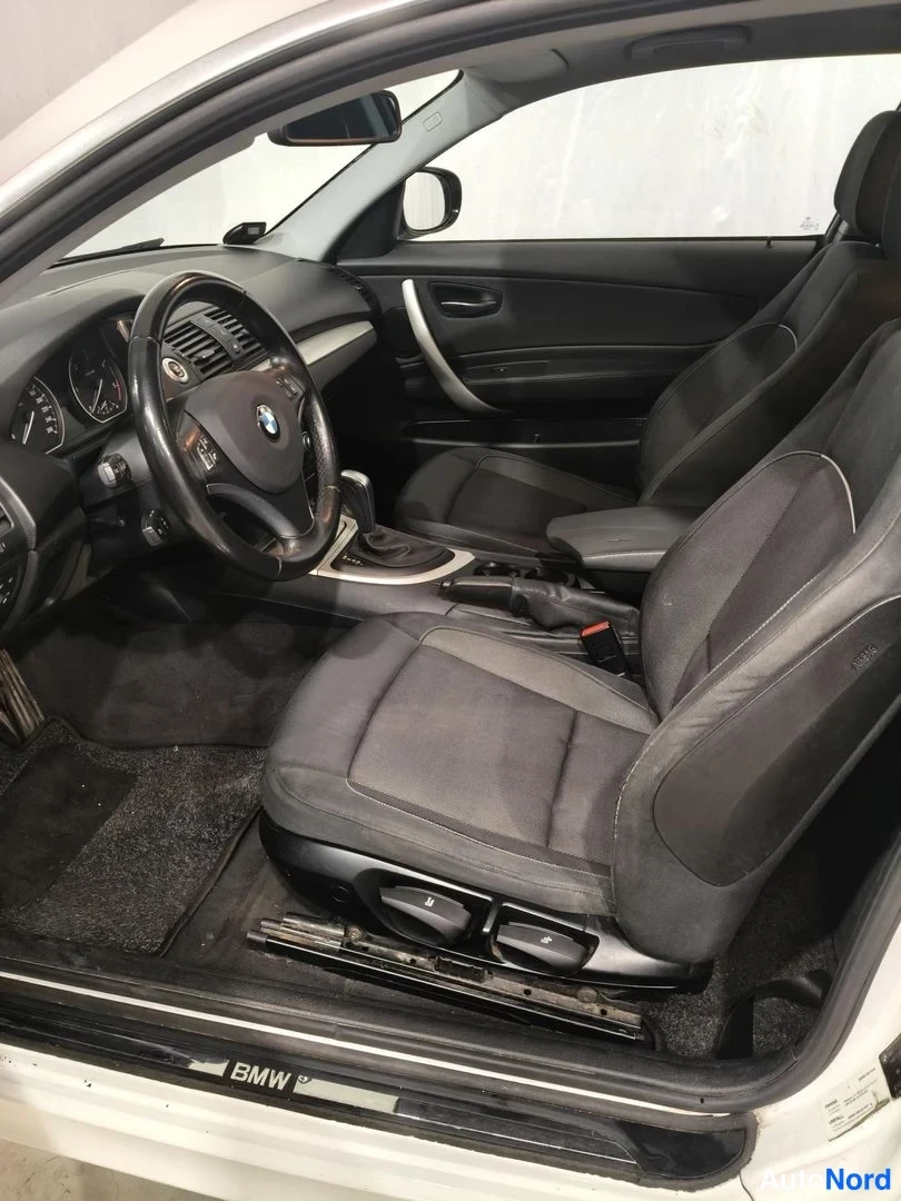 Muu: Auto-istuinten ja kojelaudan lähikuva, edessä ohjauspyörä ja vaihtajan mutteri